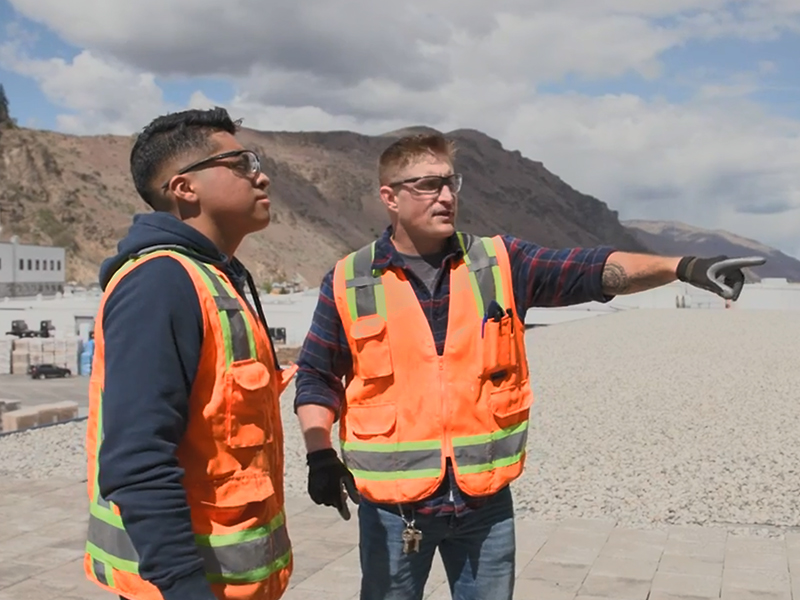 Two men in safety vest and helmets on job site.