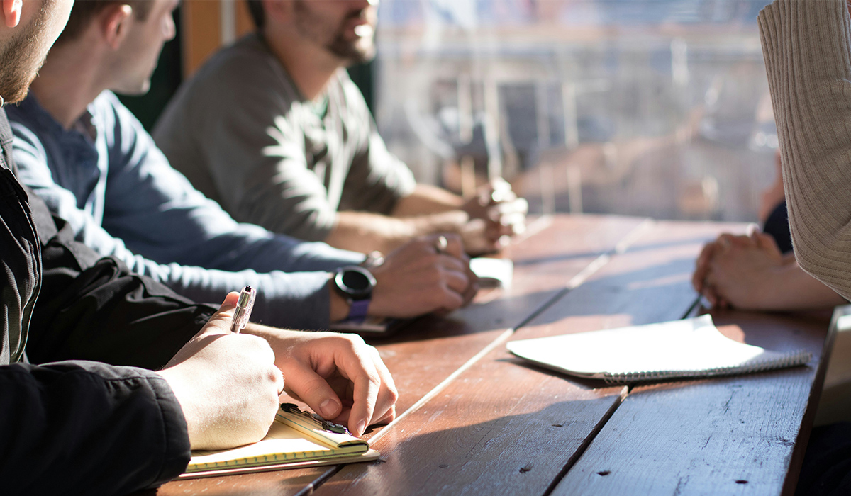A group of people sit at a table with their notebooks and pens.
