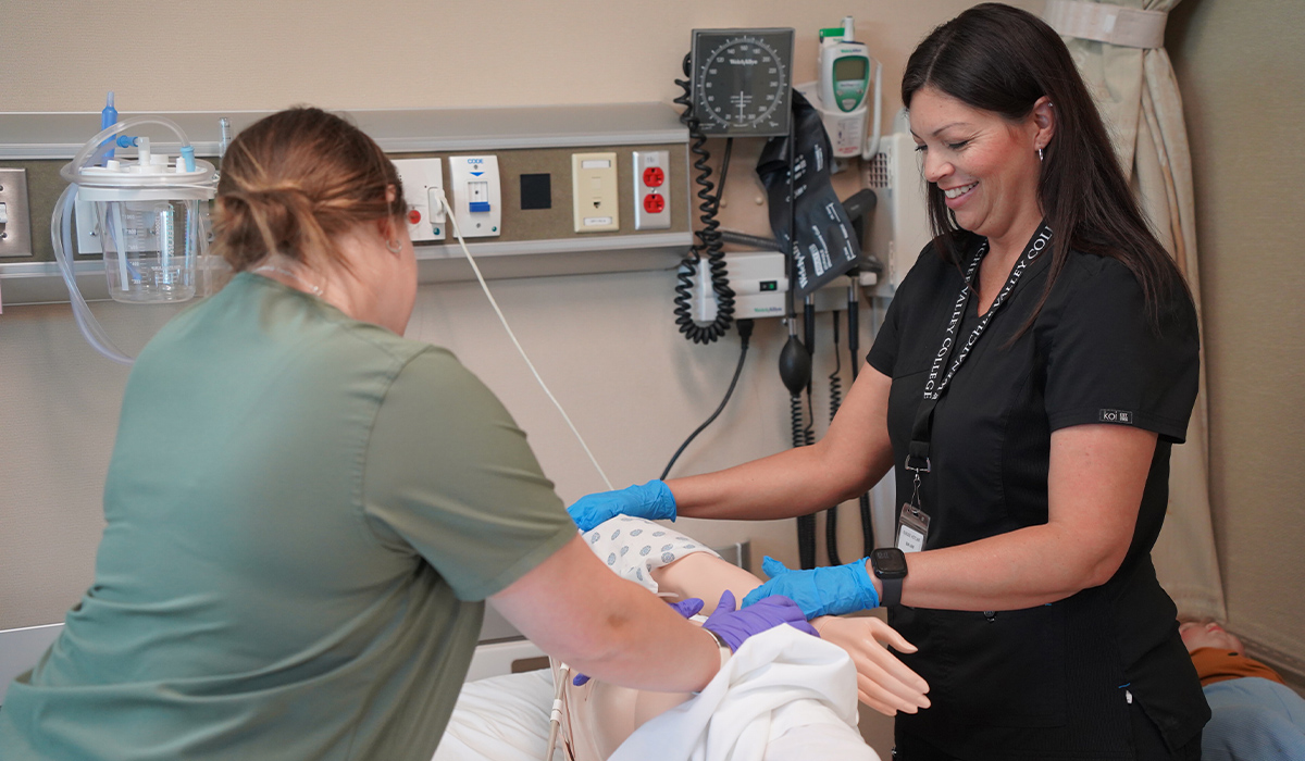 A medical assistant student and instructor roll a manikin onto its side in a hospital bed.