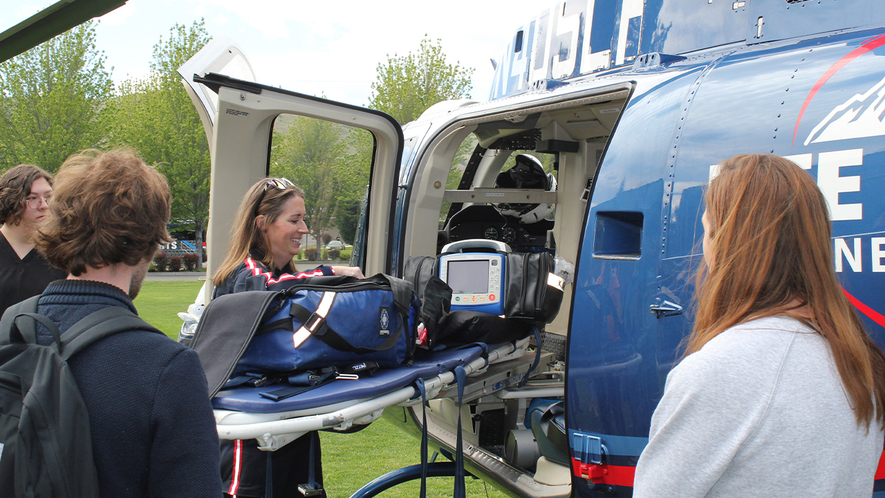 Students circle around a medivac helicopter and a nurse pulling a stretcher from the helicopter.