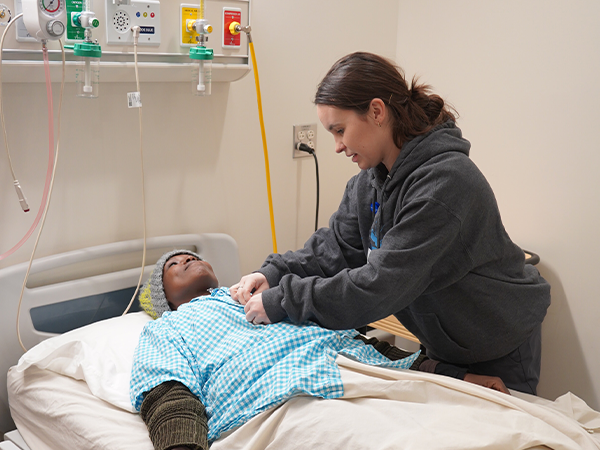 A WVC nursing assistant practices healthcare skills on another student lying in a hospital bed.