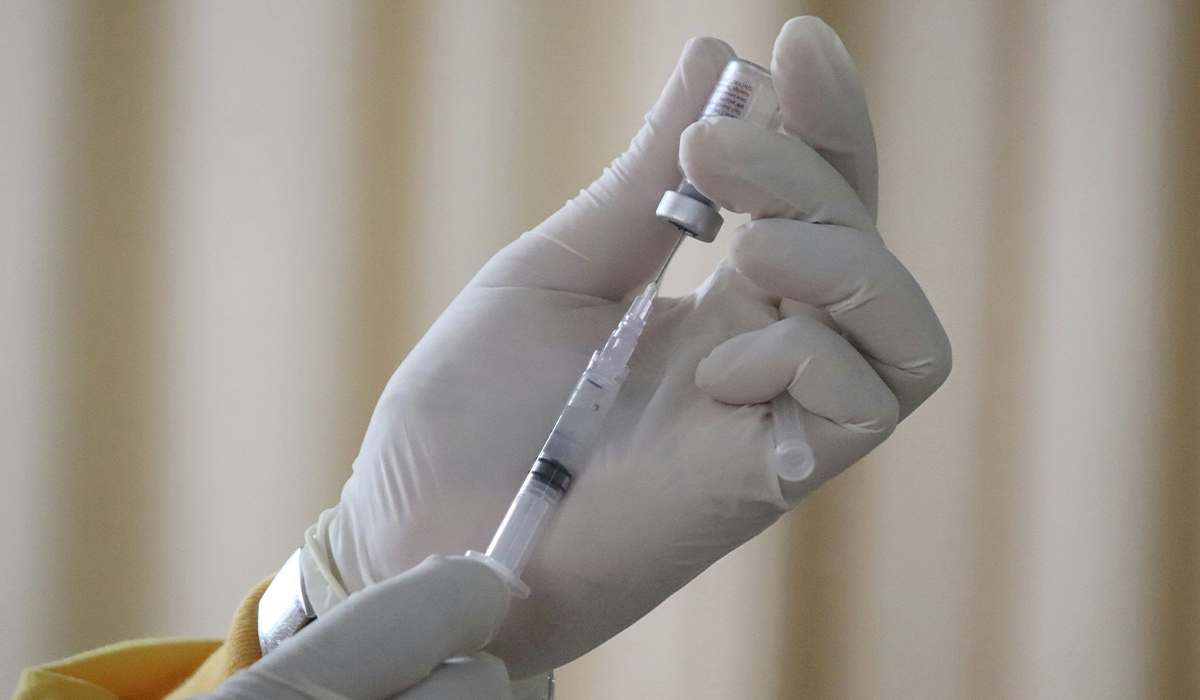 A gloved hand places a syringe into a bottle of medicine.