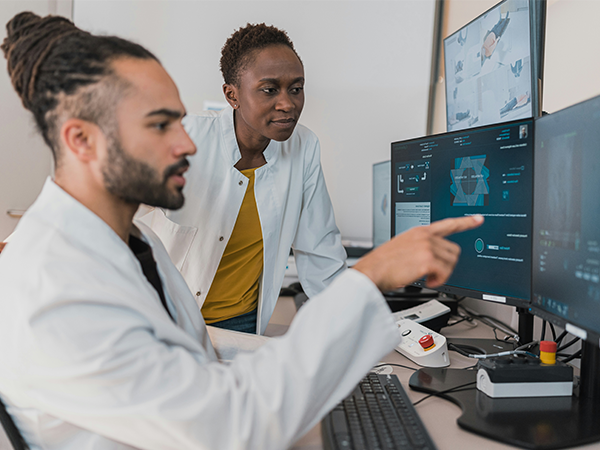 Two lab technicians study an x-ray on a computer screen.