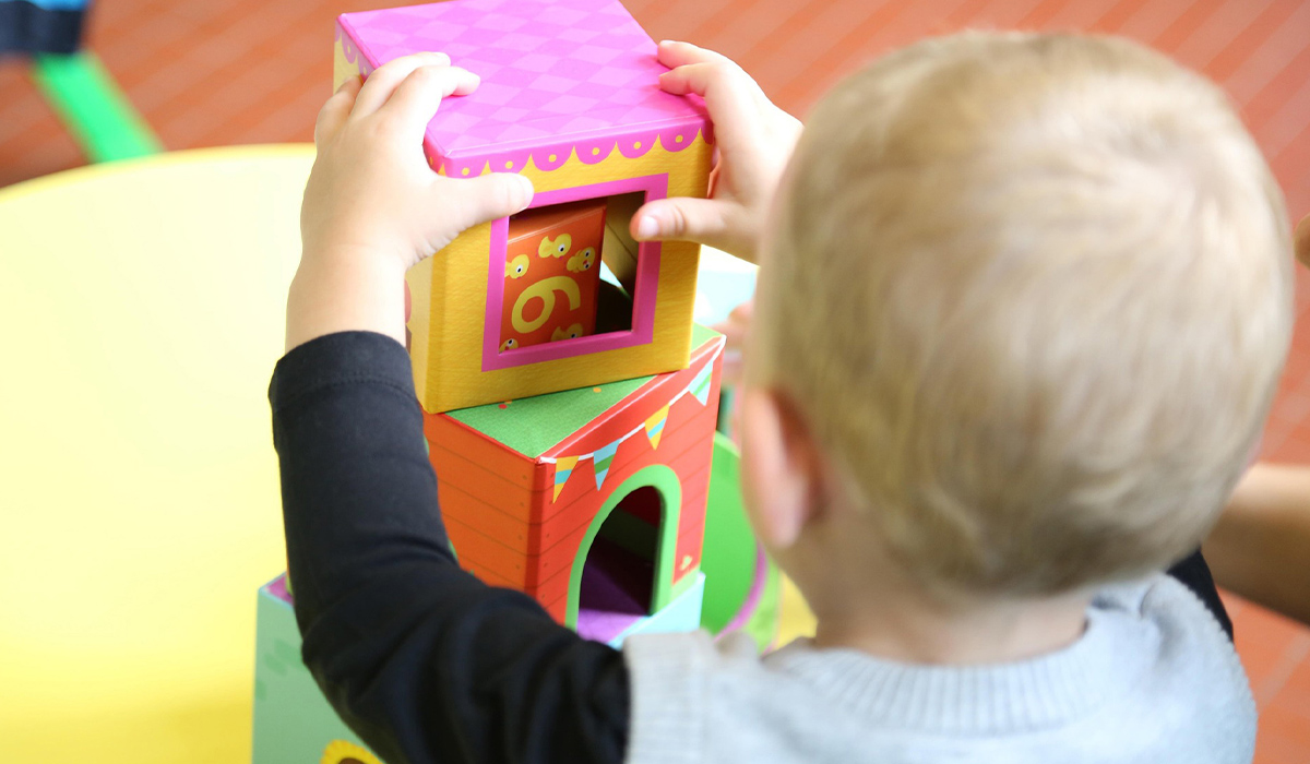 A child sits on a floor and stacks colorful blocks.
