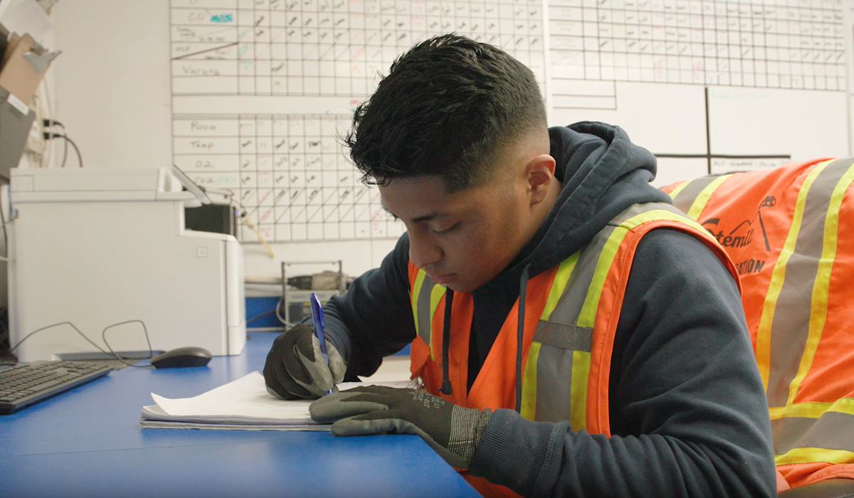 A WVC ESRT student wearing a bright orange vest and gloves sits at a desk to complete paperwork.