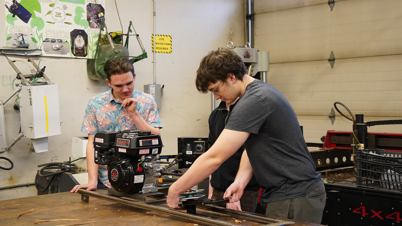 Three students work on placing a motor onto a frame.