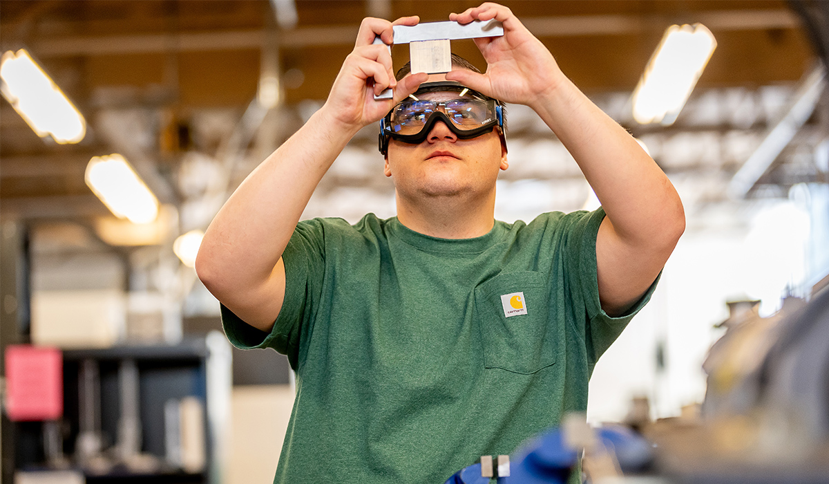 A student wearing protective gear studies his machining project.