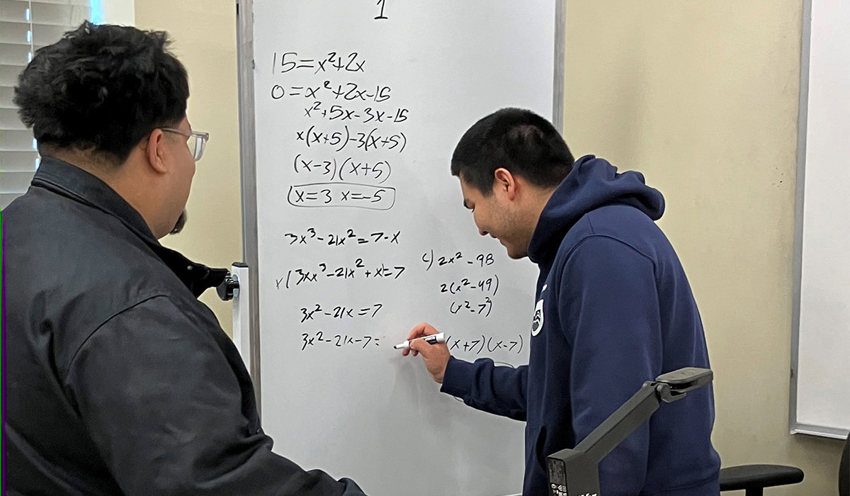 Two math students complete a math problem on a whiteboard.