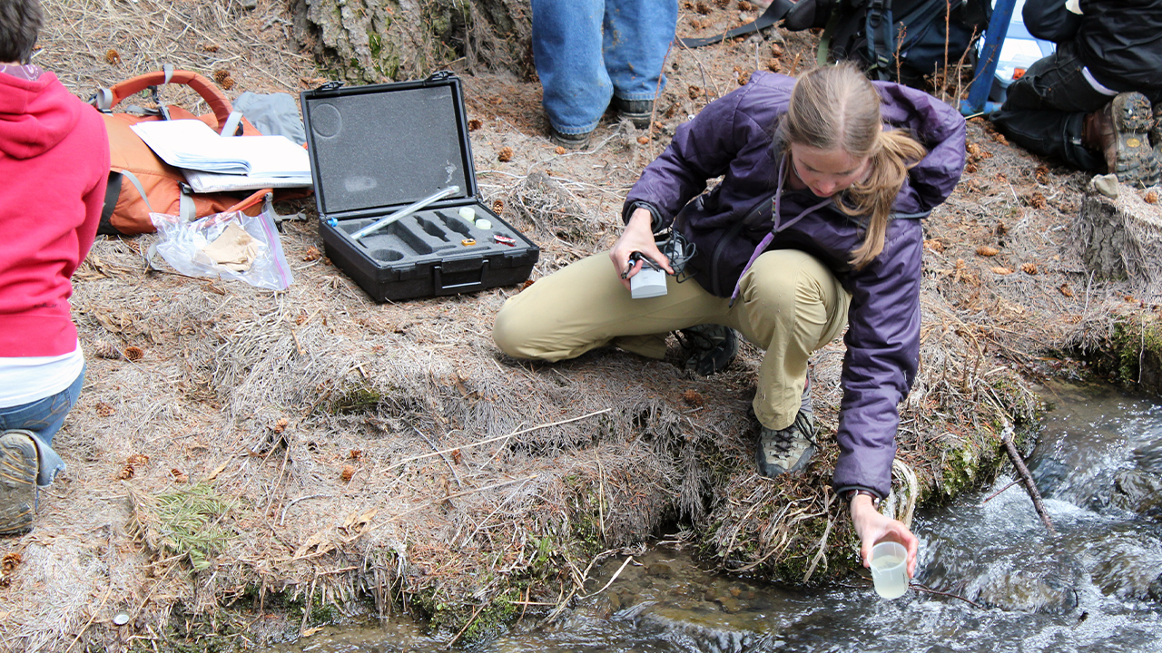 A student dips a specimen cup into a creek.