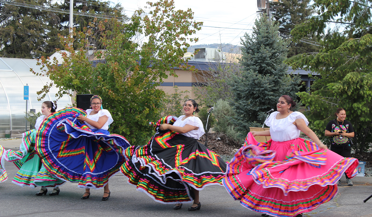 Women dressed in traditional dresses dance to mariachi music.