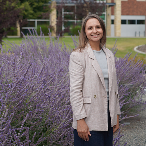 Karyna Bukovtsova standing outside by purple flowers.