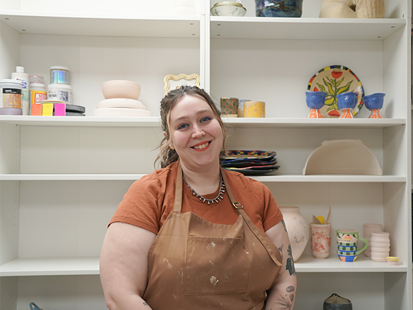 Professor Sarah Sprouse stands in front of shelves with a variety of ceramics.