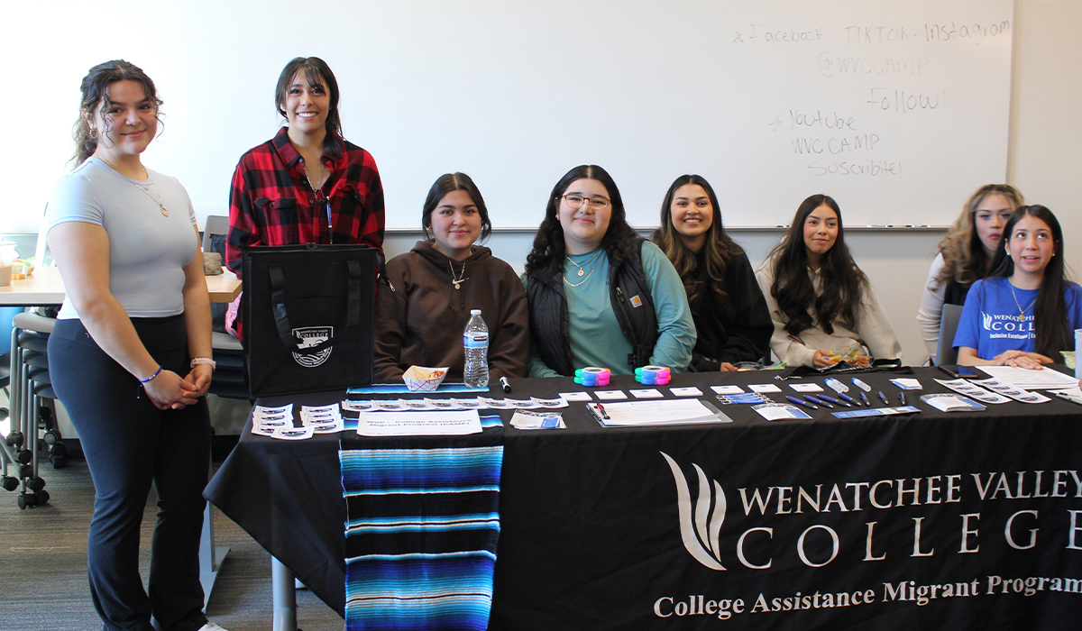 A group of CAMP students stand and sit behind a long table with a black and white WVC CAMP logo.