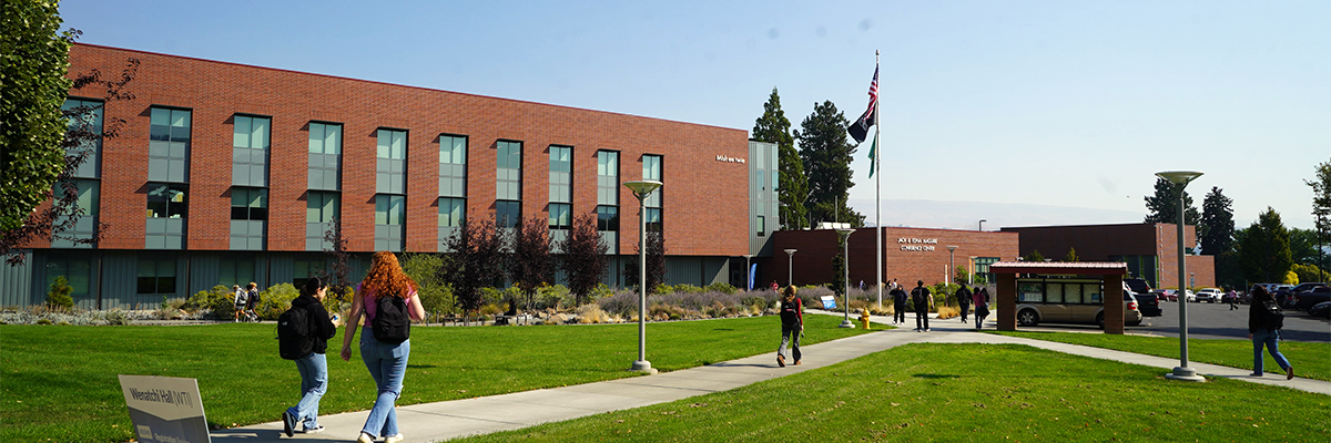 A few students walking on the sidewalk in front of the Mish ee twie building.