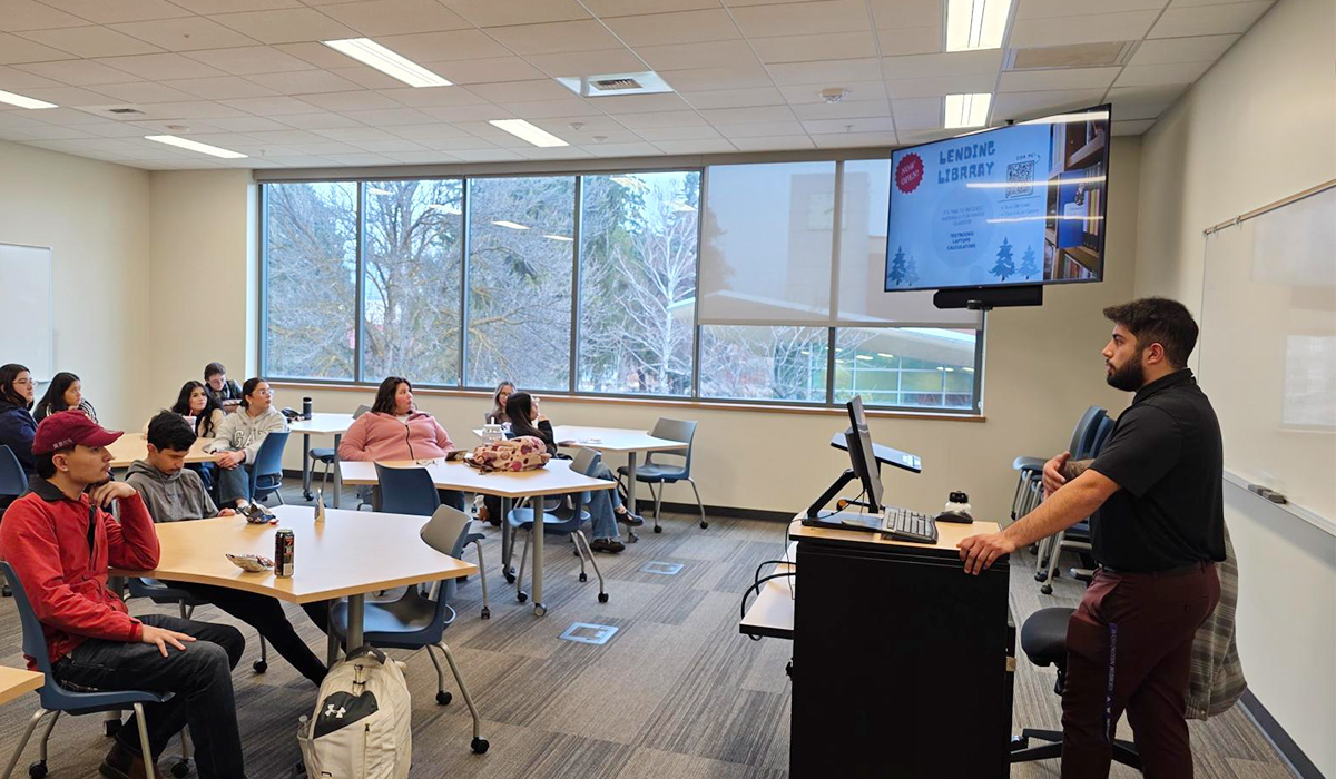 A TRIO staff member stands at the front of a classroom and speaks with students.