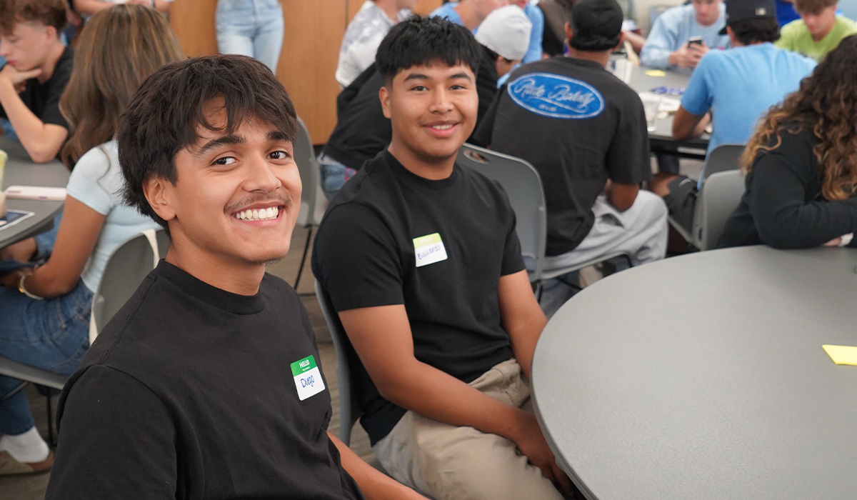Two students seated at a round table smile at the camera.